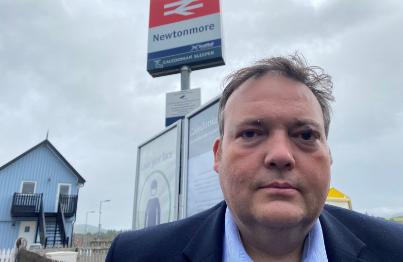 Jamie standing in front of the sign for Newtonmore Railway Station