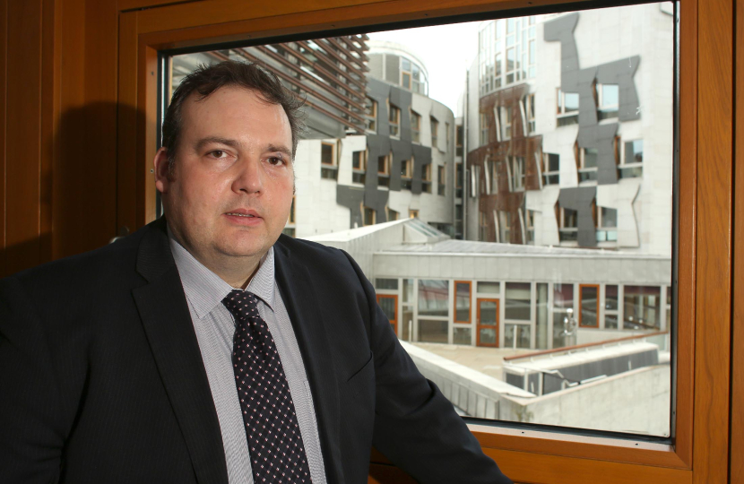 Jamie standing in front of a window overlooking the Scottish Parliament building