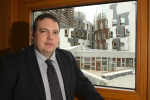 Jamie standing in front of a window overlooking the Scottish Parliament building