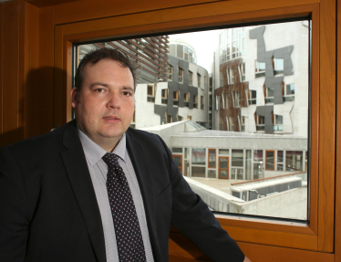 Jamie standing in front of a window overlooking the Scottish Parliament building